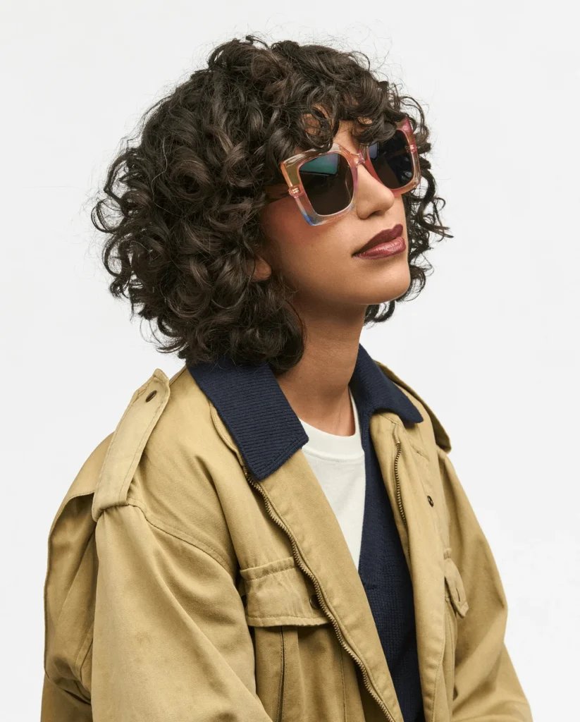 カールヘアのモデルが着用するカラーフレームのサングラス